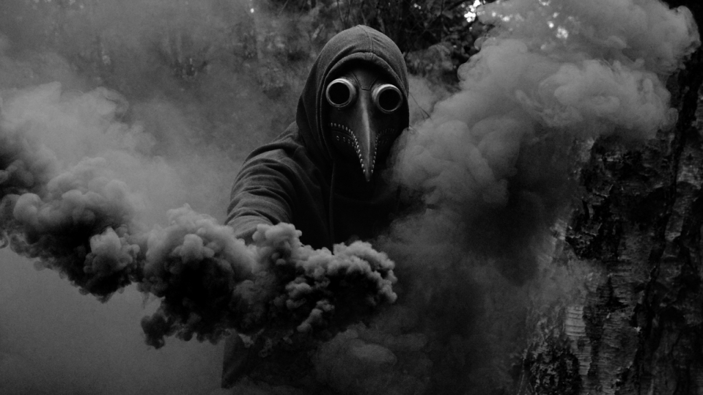 Mensch mit Vogelmaske und Kapuzenpulli umgeben von Bäumen und Rauch