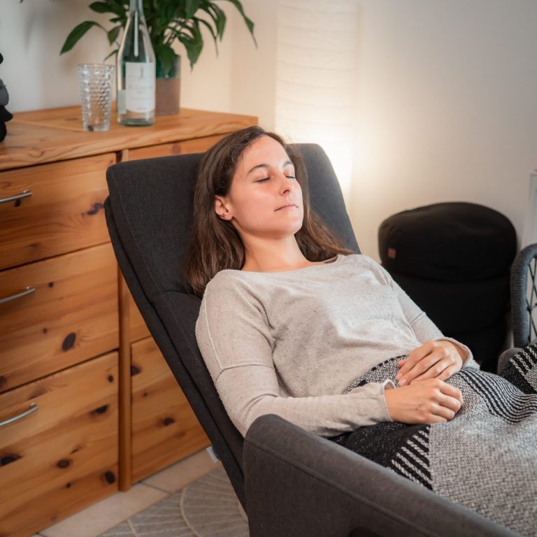 Junge Frau (Klientin) liegt mit geschlossenen Augen entspannt auf einem Relaxsessel.