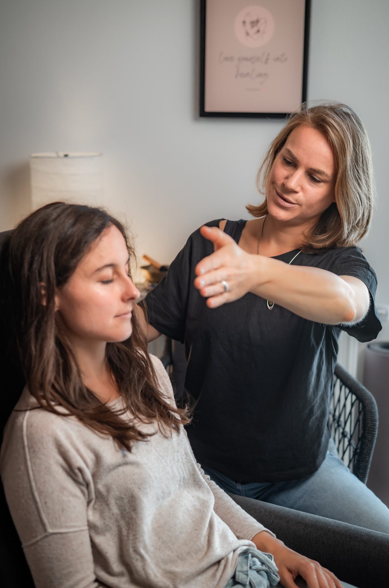 auflösende Hypnose Coaching Jasmin Kircher Rosenheim Achtsamkeit Mindfulness Meditation Buddhismus junge Frau (Klientin) sitzt mit geschlossenen Augen auf Relaxsessel. Hypnotiseurin (Jasmin Kircher) schaut sie an und bewegt ihren Arm.