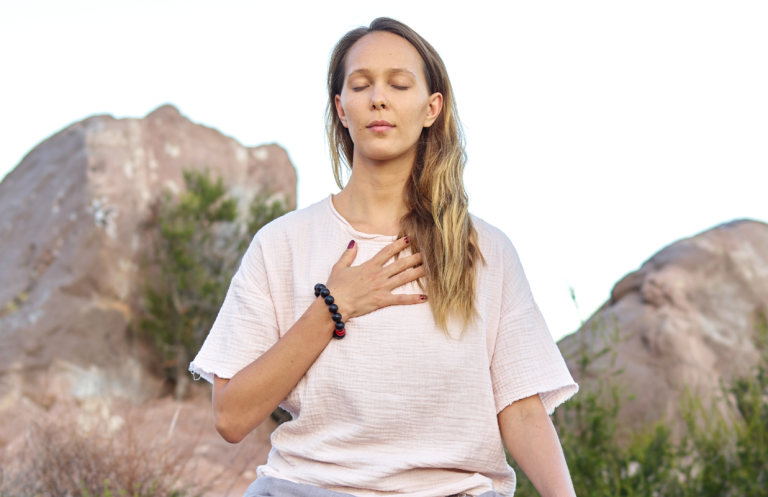 Tara Brach Meditation RAIN Achtsamkeit Mindfulness Emotional Release junge Frau meditiert mit geschlossenen Augen, hat eine Hand auf die Brust gelegt.
